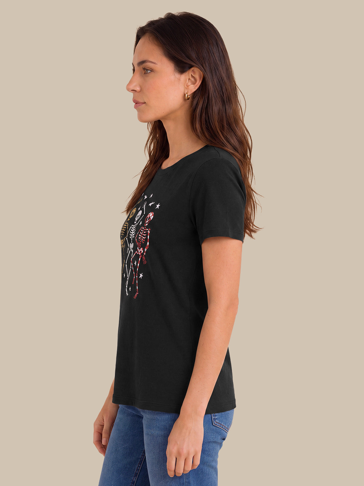 A woman in profile wearing a black short-sleeve t-shirt with a colorful graphic print on the front, paired with blue jeans, set against a solid beige background.
