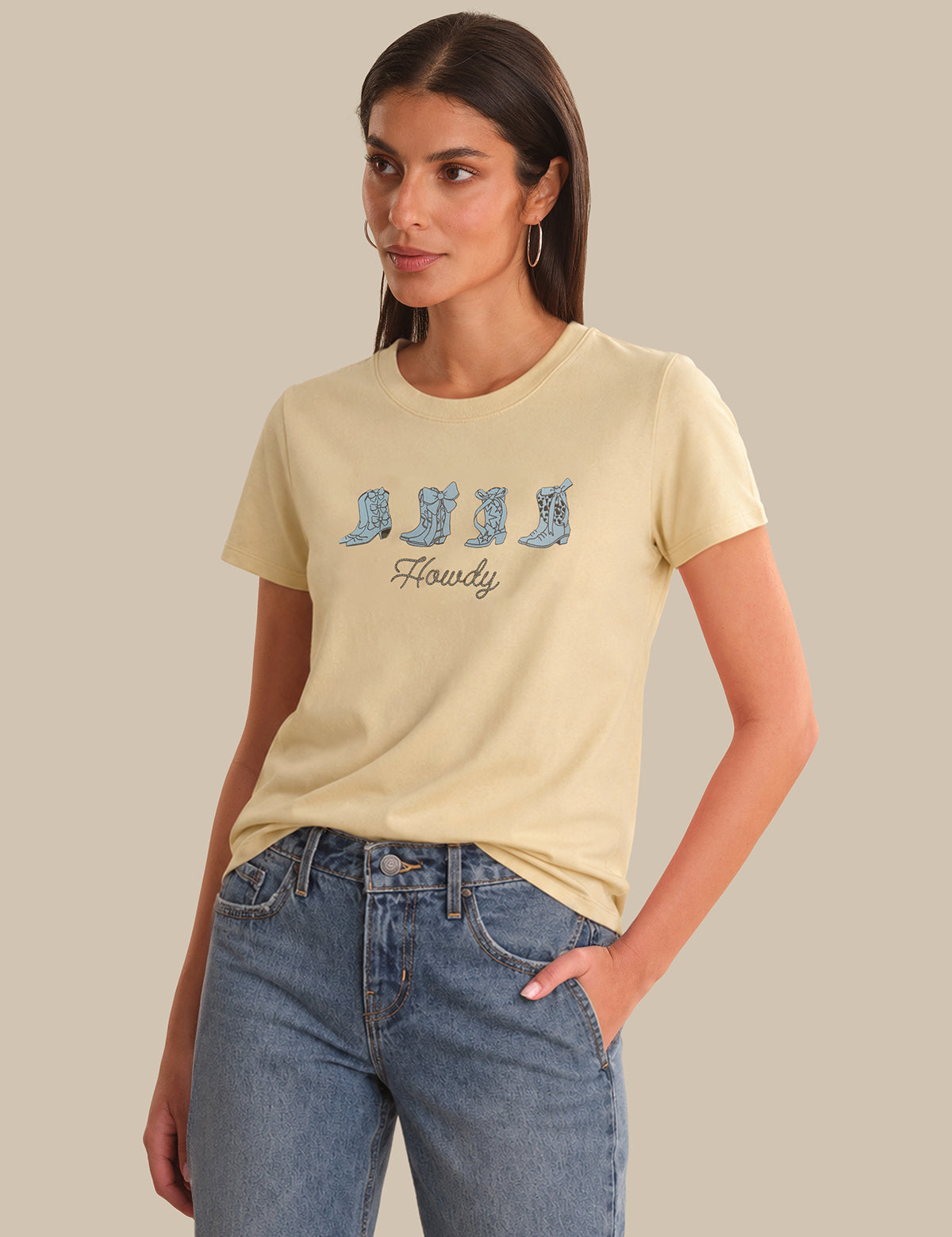 Woman wearing a beige t-shirt with a graphic design and blue jeans on a neutral background