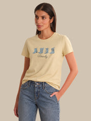 Woman wearing a beige t-shirt with a graphic design and blue jeans on a neutral background