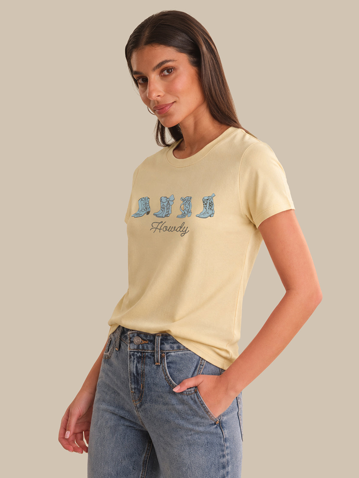 Woman wearing a light yellow t-shirt with blue boot graphic and text, standing against a plain background.