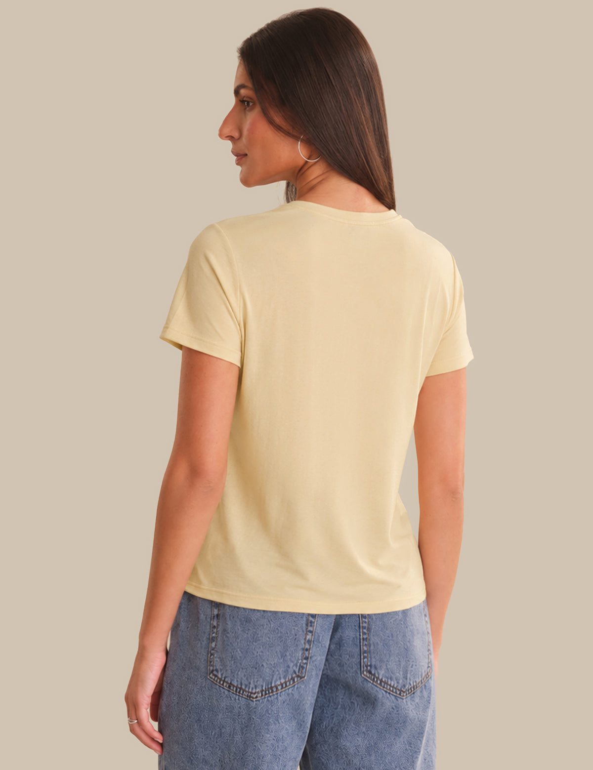 Woman wearing a light yellow t-shirt and blue jeans against a beige background
