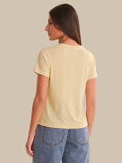 Woman wearing a light yellow t-shirt and blue jeans against a beige background
