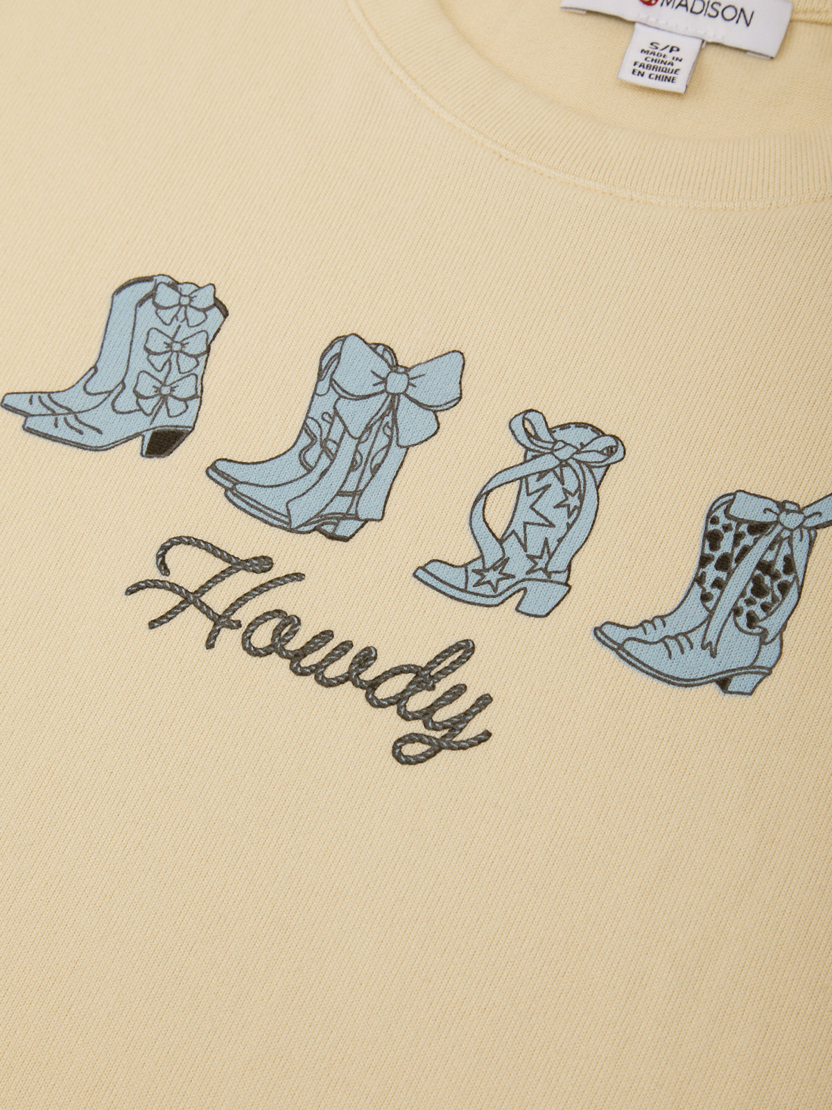 Beige t-shirt with blue cowboy boot designs and 'Howdy' text on a plain background