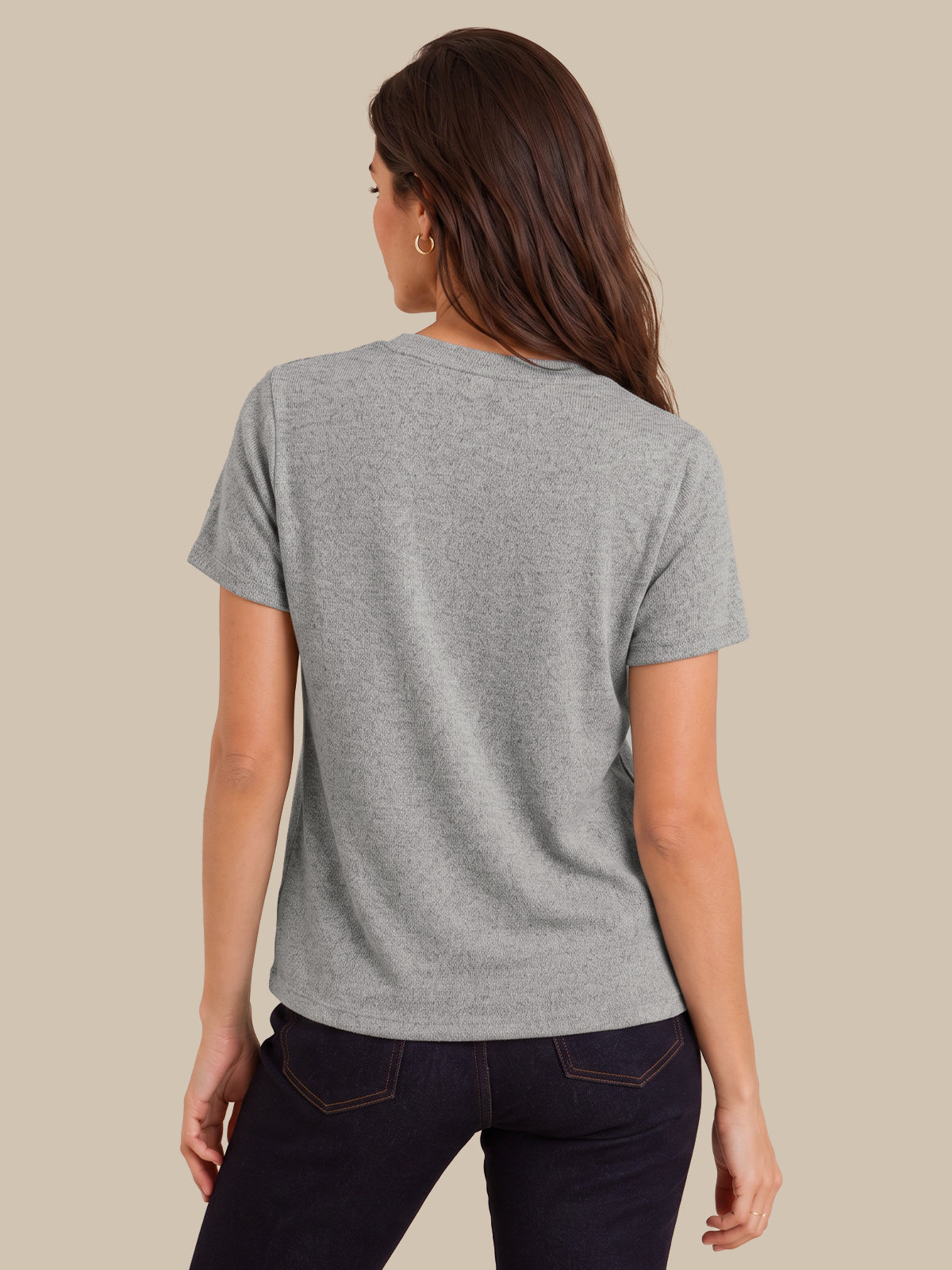 A woman shown from the back wearing a heather gray short-sleeve t-shirt and dark jeans, set against a solid beige background.