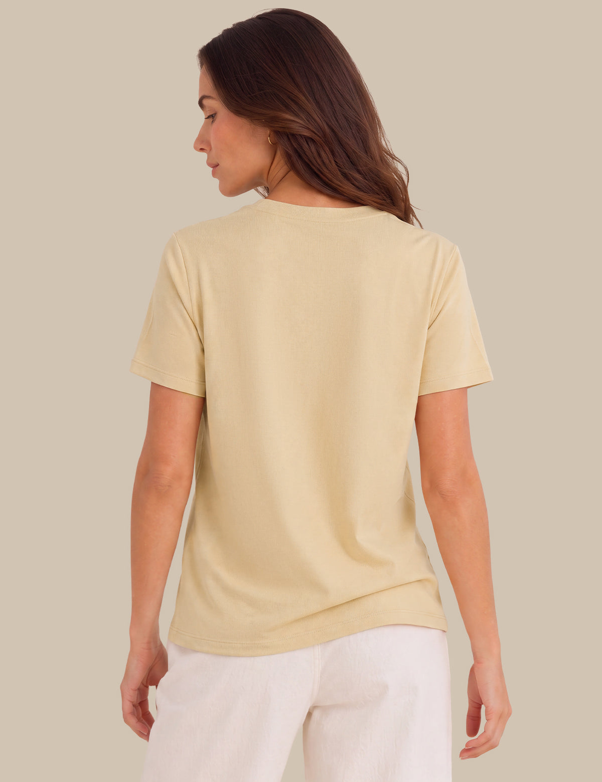 A woman shown from the back wearing a pale cream-colored short-sleeve t-shirt and white pants, set against a solid light beige background.