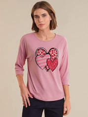 Woman wearing a pink long-sleeve top with heart designs on a beige background