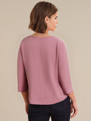 Woman wearing a mauve long-sleeve top against a beige background