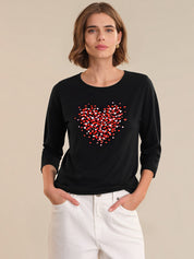 Woman wearing a black long-sleeve shirt with a red heart design on a beige background