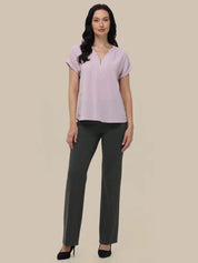 Woman wearing a light purple blouse and dark gray pants on a beige background