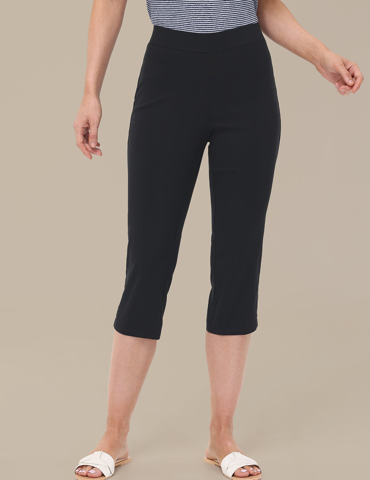 Person wearing black capri pants on a beige background