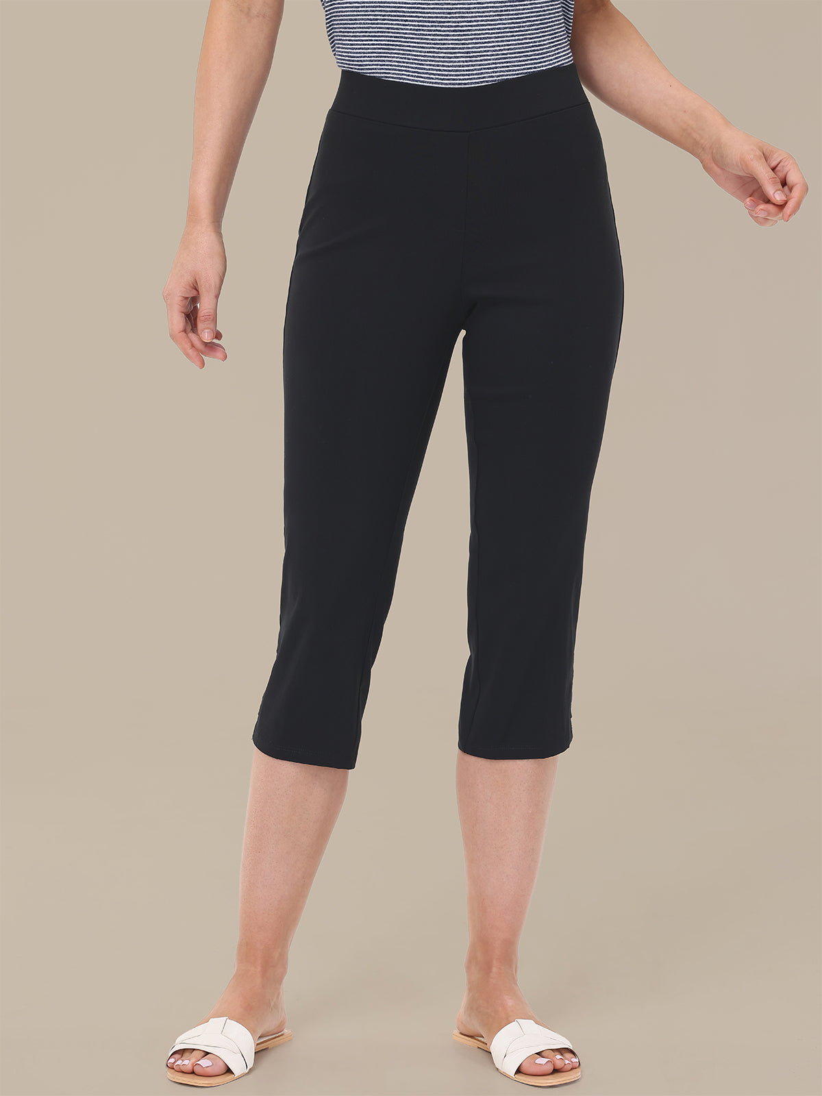 Person wearing black capri pants on a beige background