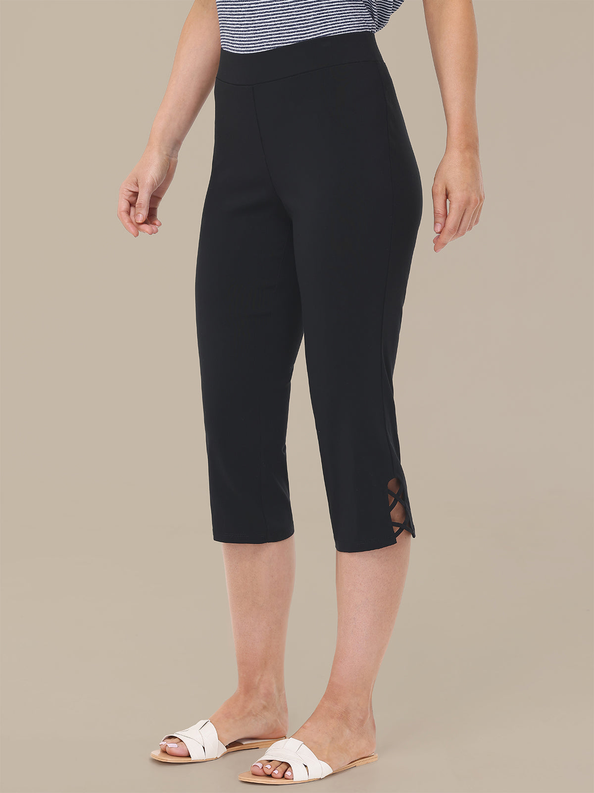 Person wearing black capri pants with a beige background
