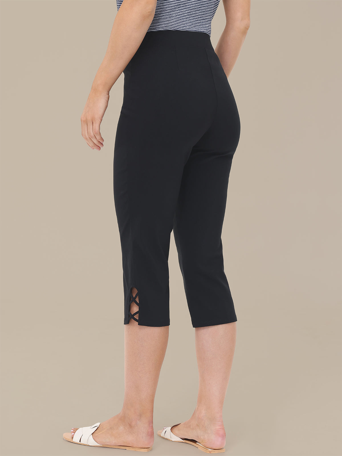 Person wearing black capri pants with cut-out details on a beige background
