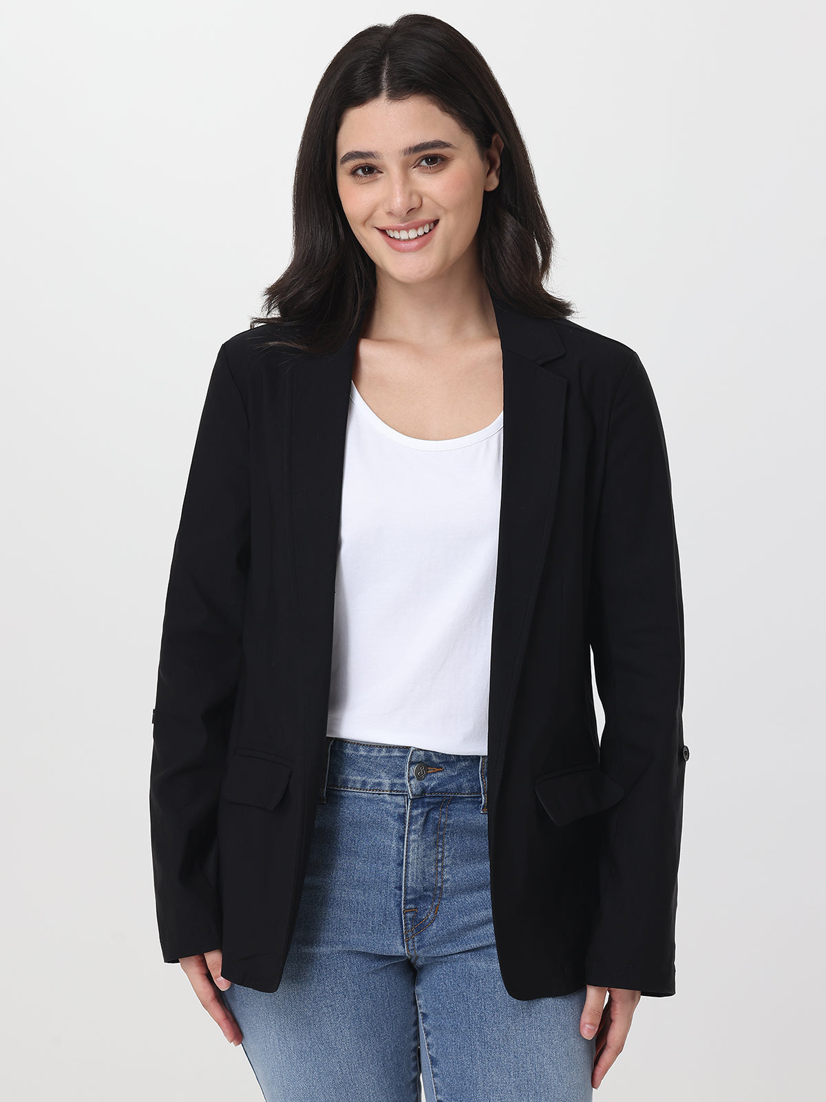 Woman wearing a black blazer over a white top and blue jeans on a light gray background