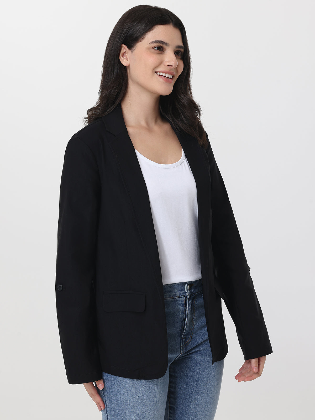 Woman wearing a black blazer over a white top and blue jeans on a white background