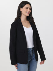 Woman wearing a black blazer over a white top and blue jeans on a white background
