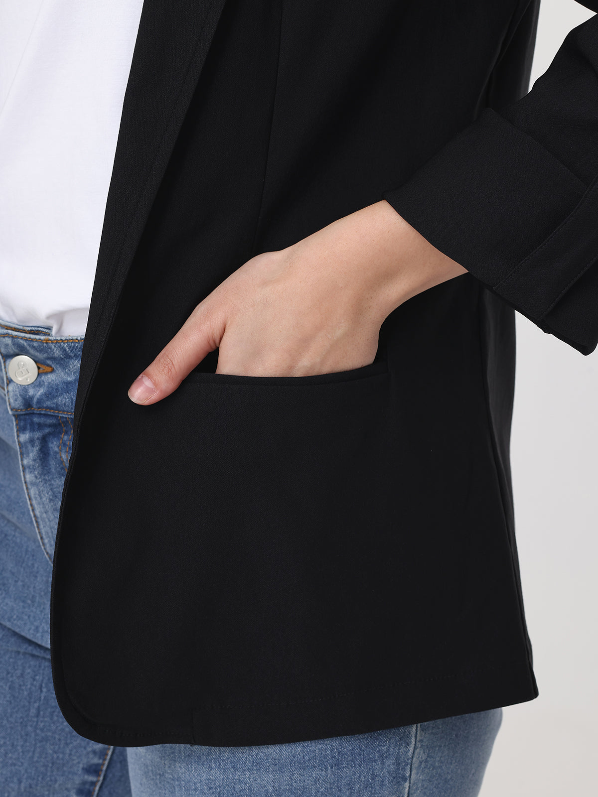 Person wearing a black blazer with a white shirt and blue jeans on a light gray background