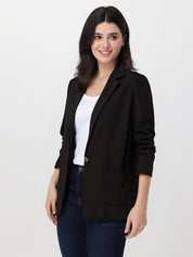 Woman wearing a black blazer over a white top and blue jeans on a white background