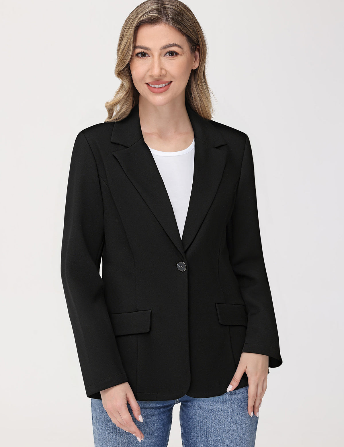 Woman wearing a black blazer over a white shirt and blue jeans on a light gray background