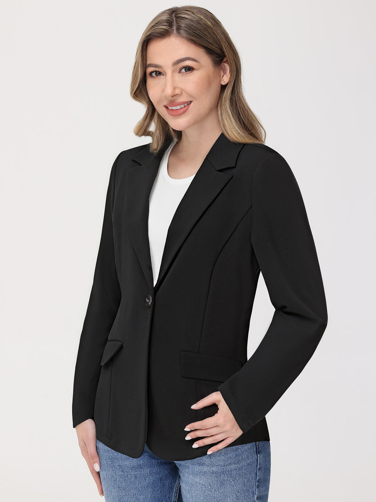 Woman wearing a black blazer over a white shirt with blue jeans on a light gray background