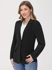 Woman wearing a black blazer over a white shirt with blue jeans on a light gray background