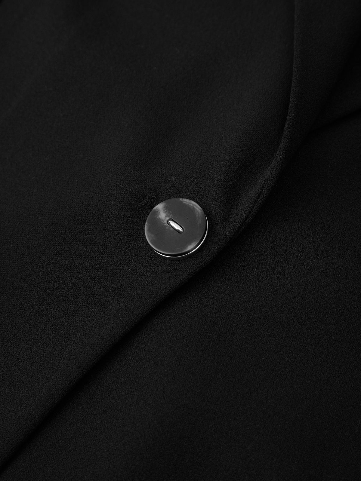 Close-up of a black coat with a button on a plain background