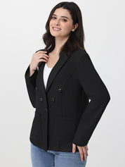 Woman wearing a black blazer over a white top and blue jeans on a light gray background