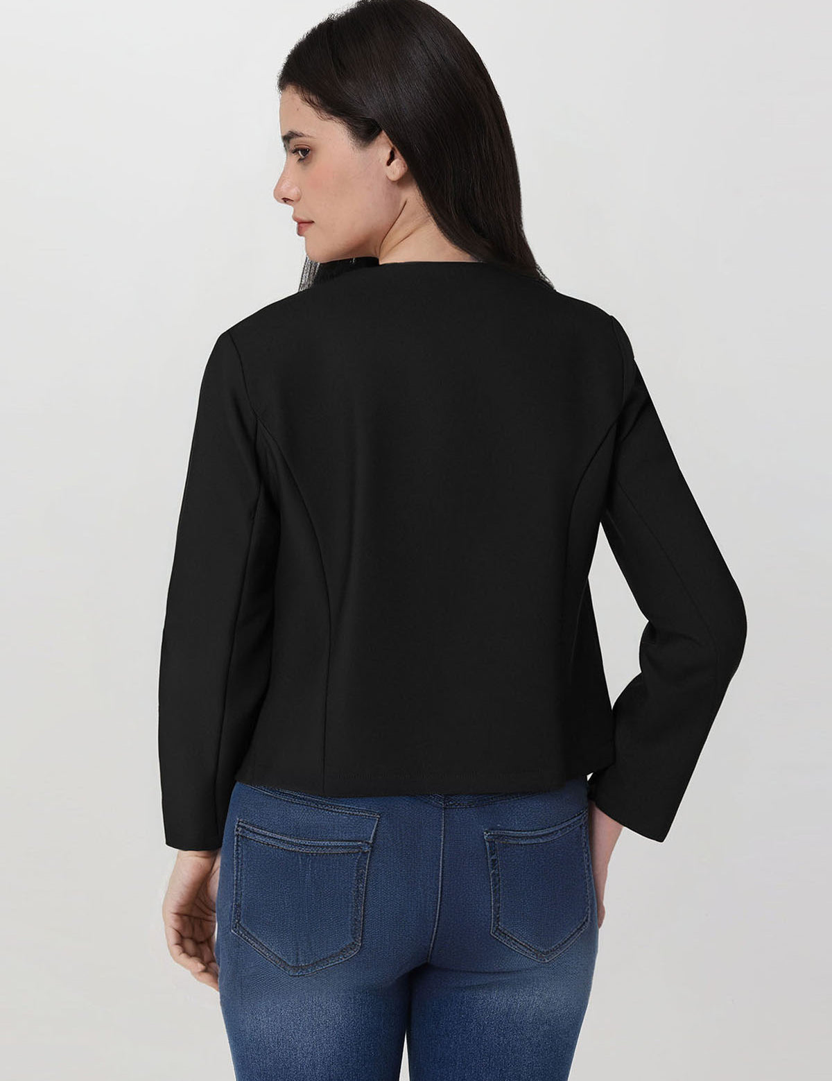 Woman wearing a black jacket and blue jeans on a plain background