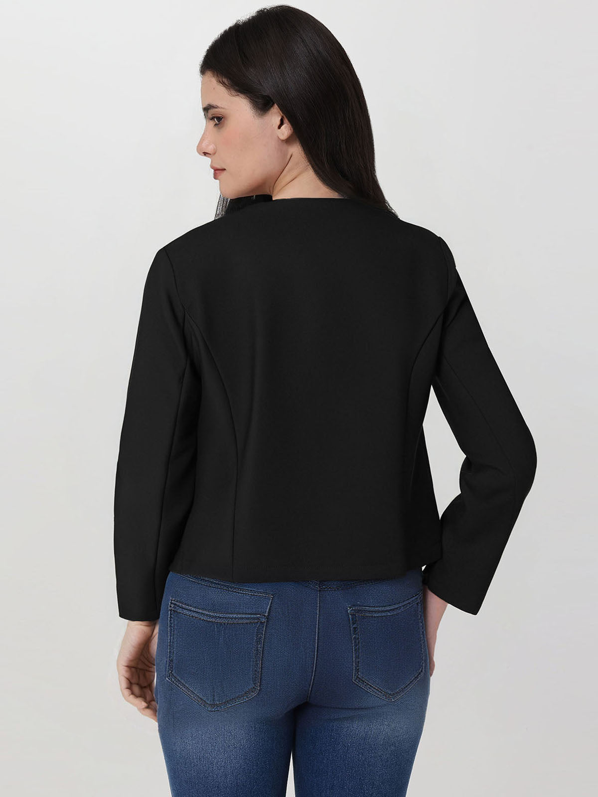 Woman wearing a black jacket and blue jeans on a plain background