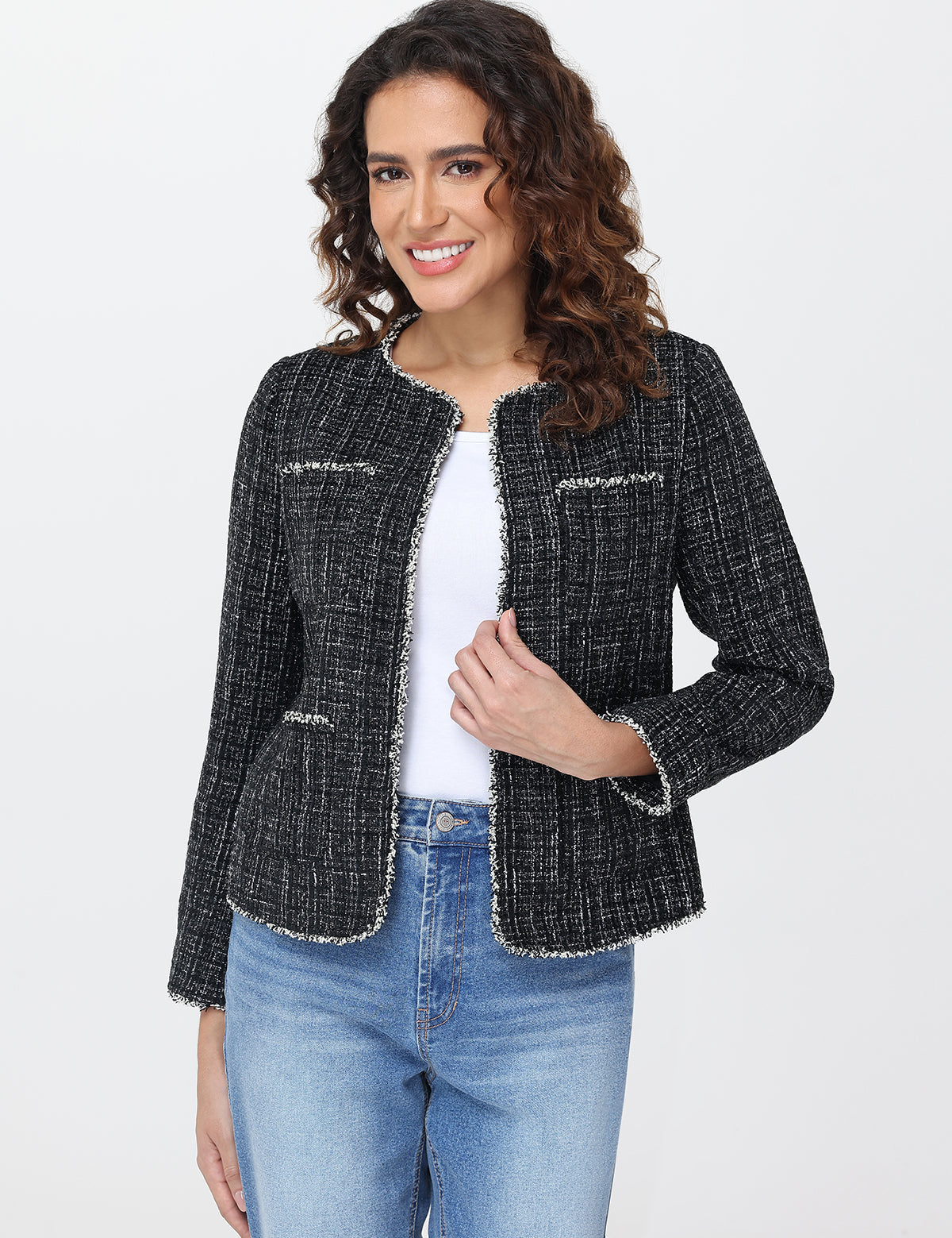 Woman wearing a black tweed jacket over a white shirt and blue jeans on a light gray background