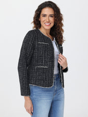 Woman wearing a black and white patterned jacket over a gray top and blue jeans on a light gray background