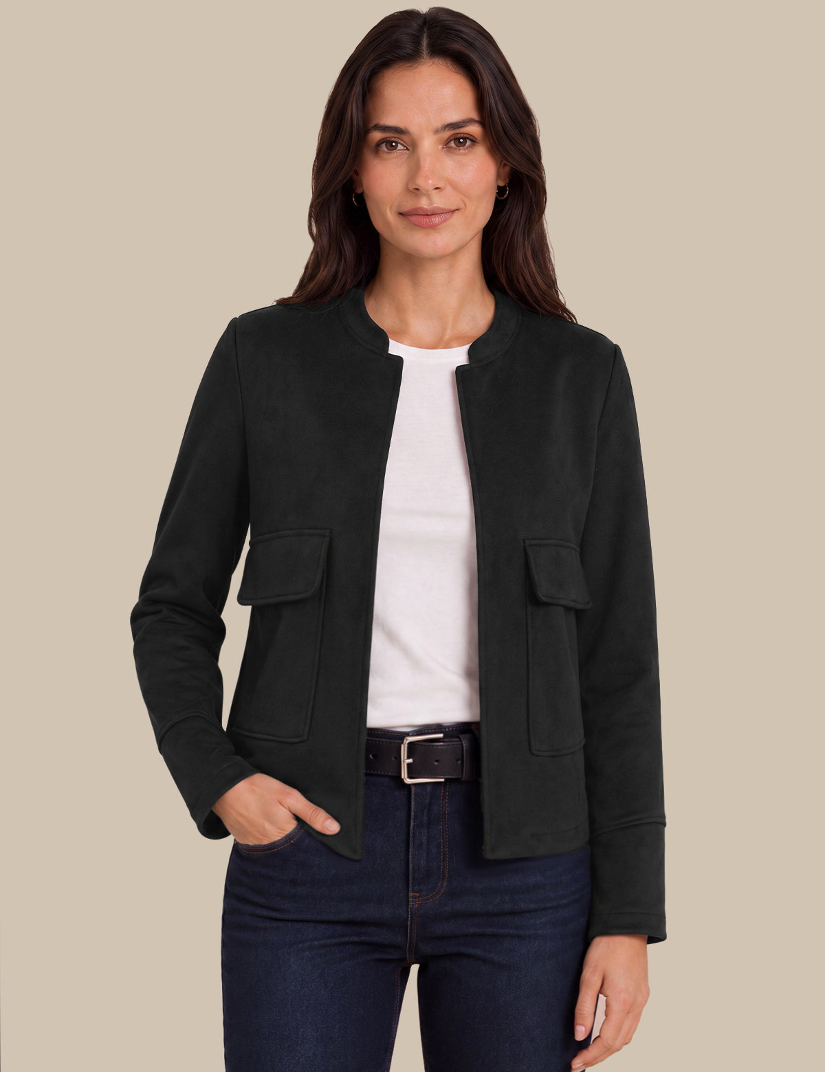 A woman modeling a black cropped jacket with flap pockets over a white top and dark blue jeans, set against a solid beige background.