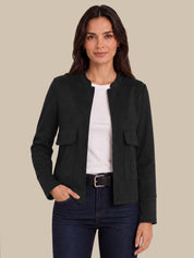 A woman modeling a black cropped jacket with flap pockets over a white top and dark blue jeans, set against a solid beige background.