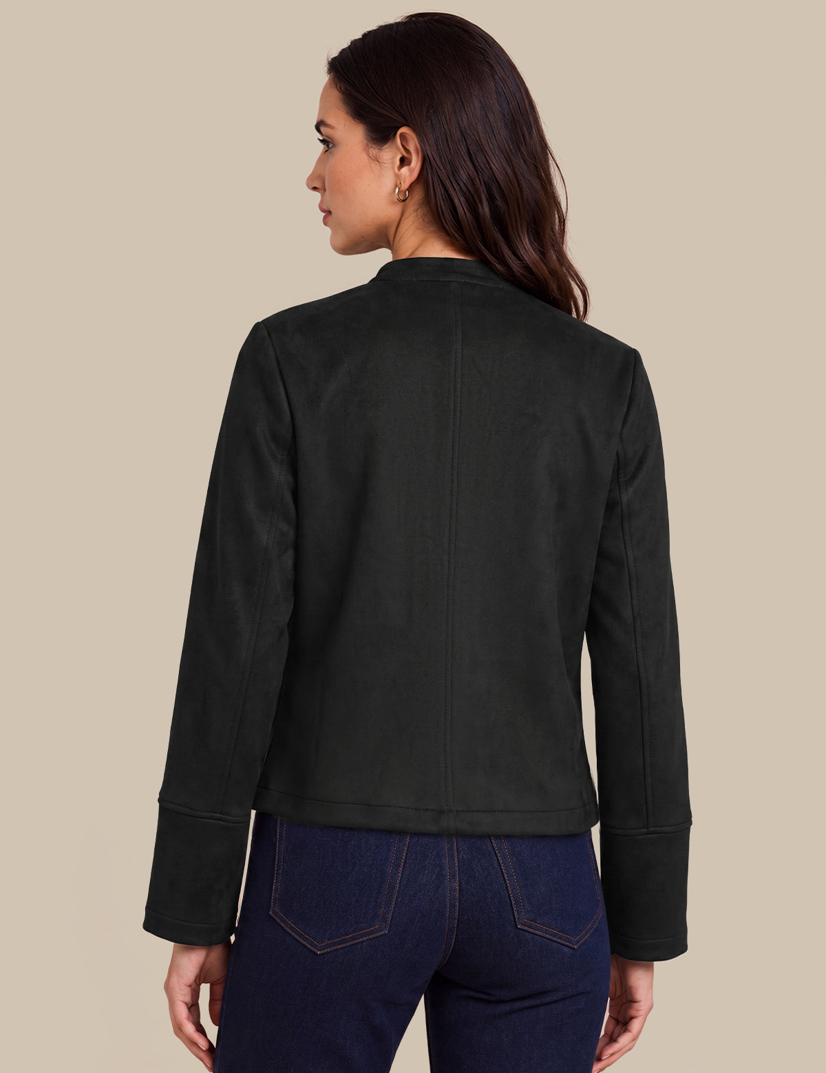 A woman shown from the back wearing a black cropped jacket and dark blue jeans, photographed against a solid beige studio background.