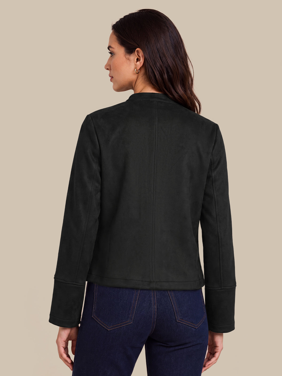 A woman shown from the back wearing a black cropped jacket and dark blue jeans, photographed against a solid beige studio background.