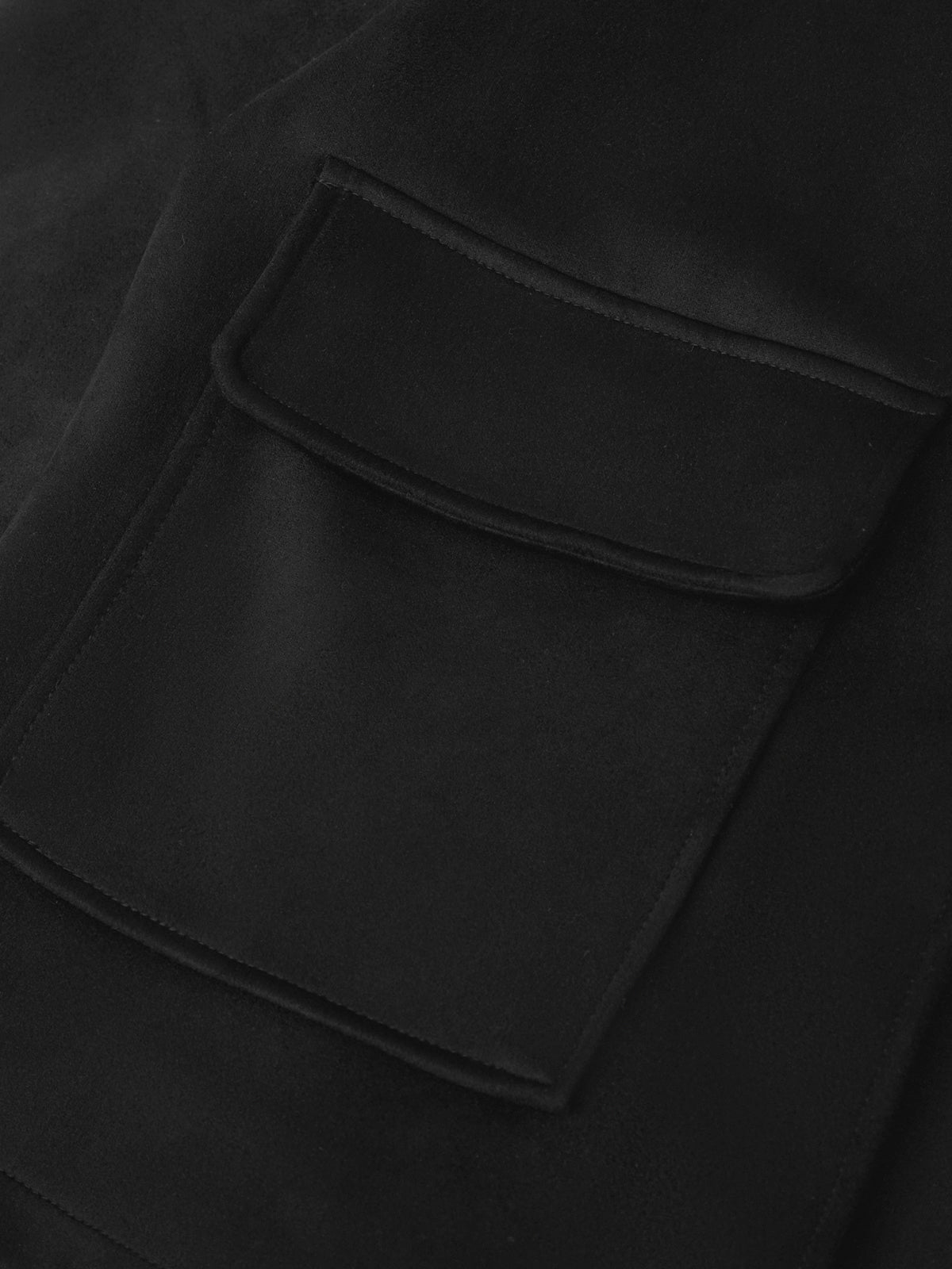 Close-up of a black fabric garment showing a large rectangular patch pocket with a curved top flap and matching black stitching.