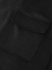 Close-up of a black fabric garment showing a large rectangular patch pocket with a curved top flap and matching black stitching.