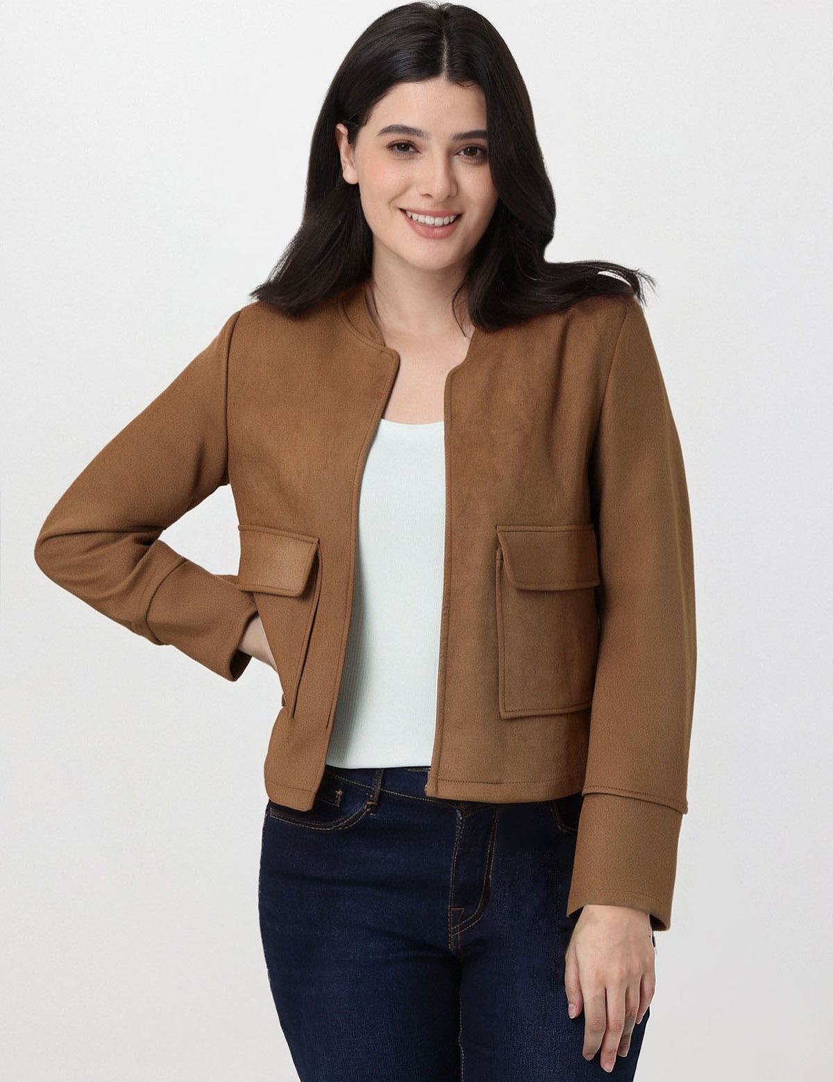 Woman wearing a brown jacket over a white top and dark jeans on a white background