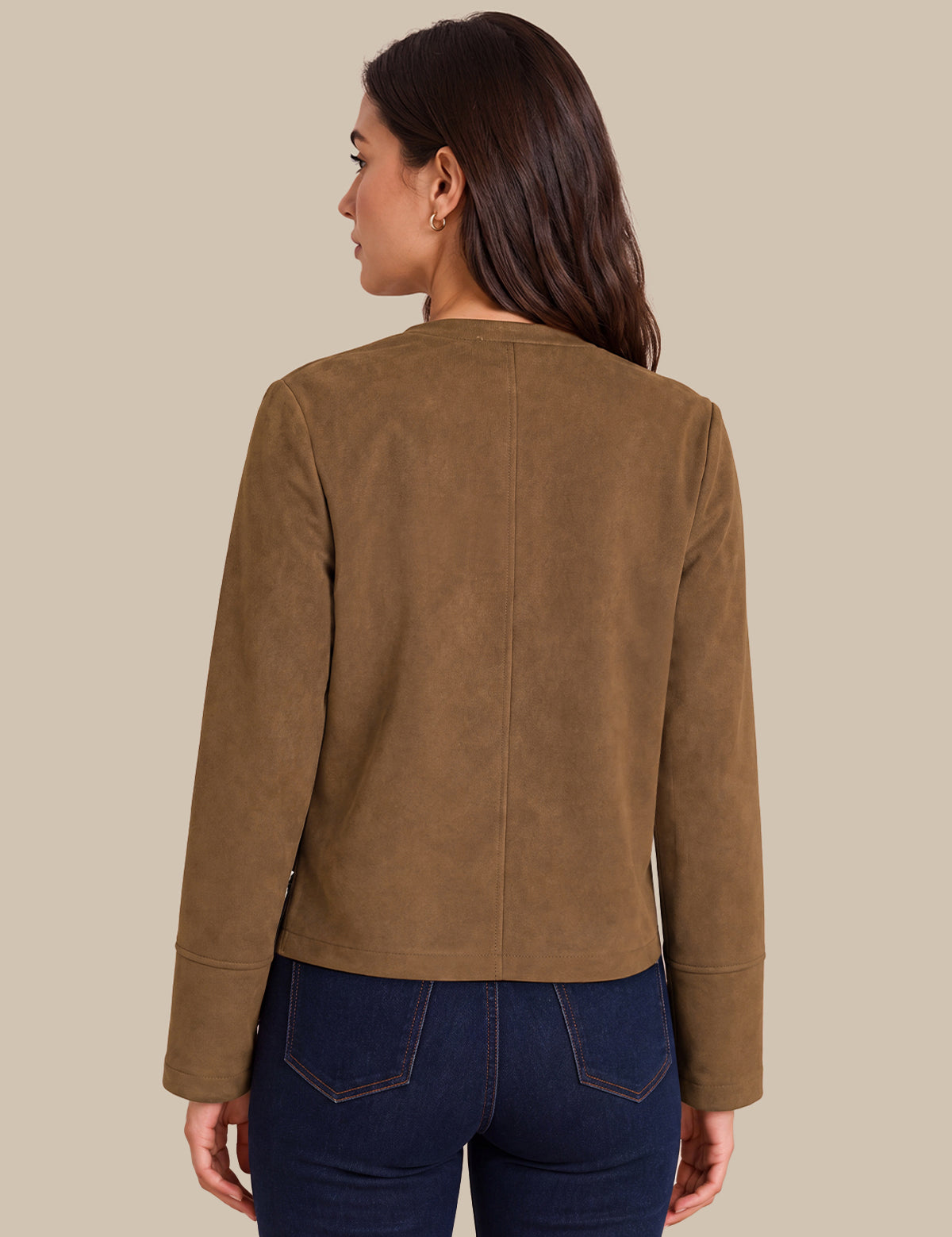 A woman shown from the back wearing a cropped, long-sleeve brown suede or faux-suede jacket and dark blue jeans, set against a solid beige background.