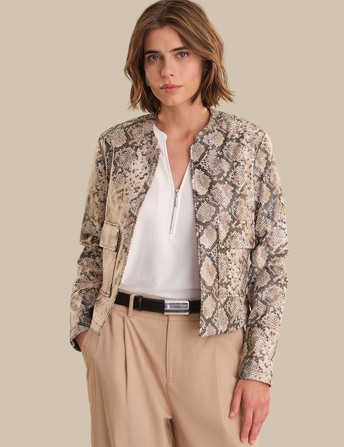 Woman wearing a snake print jacket over a white top and beige pants on a beige background