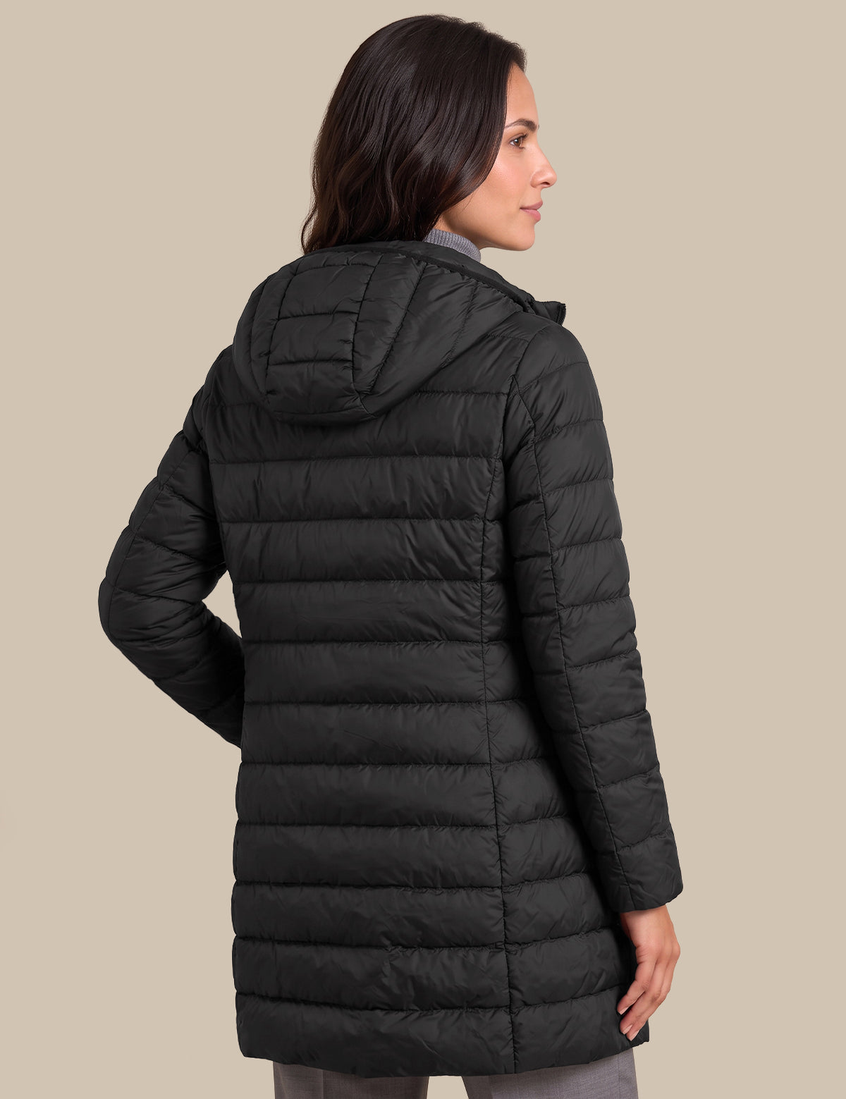 A woman shown from the back wearing a black hooded puffer jacket against a solid beige studio background.