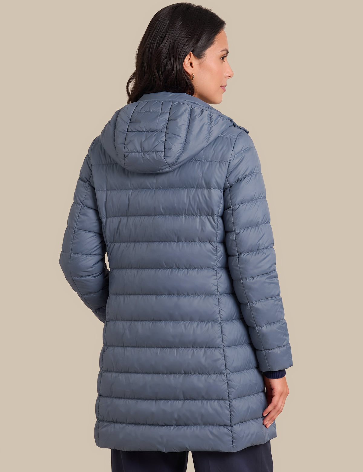 A woman shown from the back wearing a slate blue hooded puffer jacket against a solid beige background.