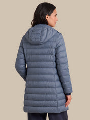 A woman shown from the back wearing a slate blue hooded puffer jacket against a solid beige background.