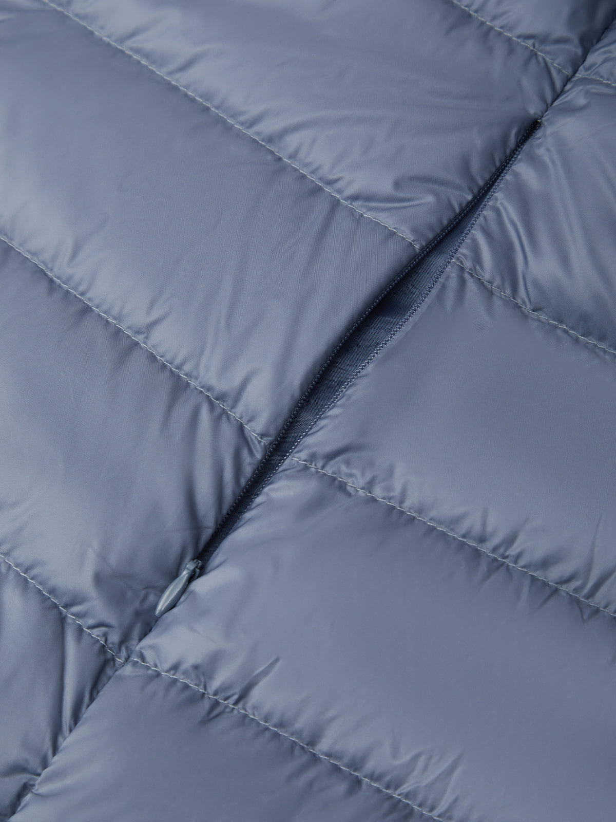 Close-up of a quilted puffer jacket in a muted slate blue-gray color, showing the texture and stitching details.