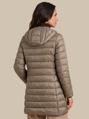 A woman shown from the back wearing a hooded puffer jacket in a taupe-beige color, photographed against a solid light beige studio background.