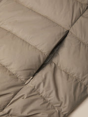 Close-up of a quilted puffer jacket in a warm taupe-beige color, showing the texture of the fabric and a black zipper running vertically.