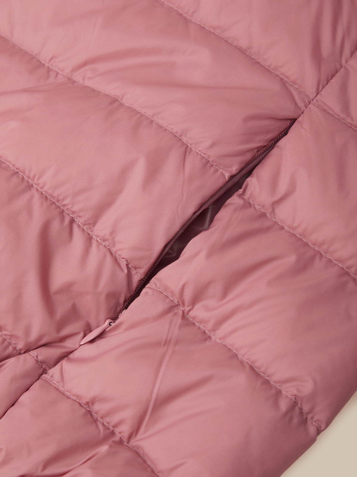 Close-up of a dusty pink puffer jacket showing the quilted stitching and a dark zipper running diagonally through the center.