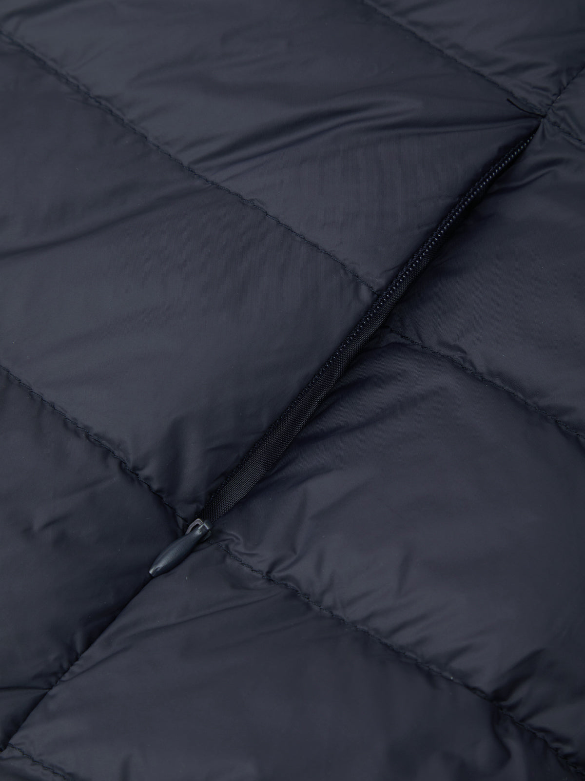 Close-up of a dark navy quilted puffer jacket showing the texture of the fabric and a black zipper detail.