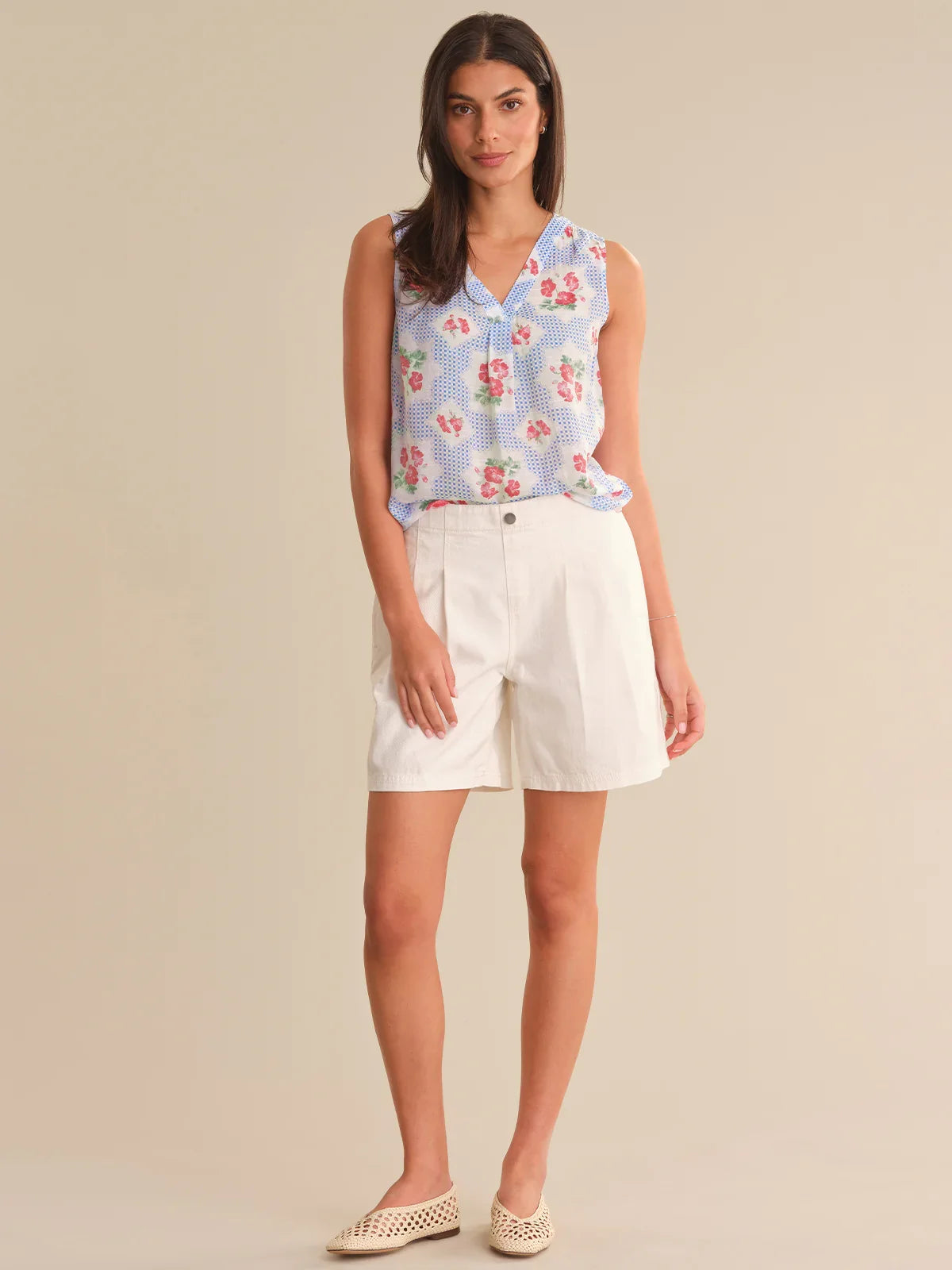 Woman wearing a floral sleeveless top and white shorts on a beige background