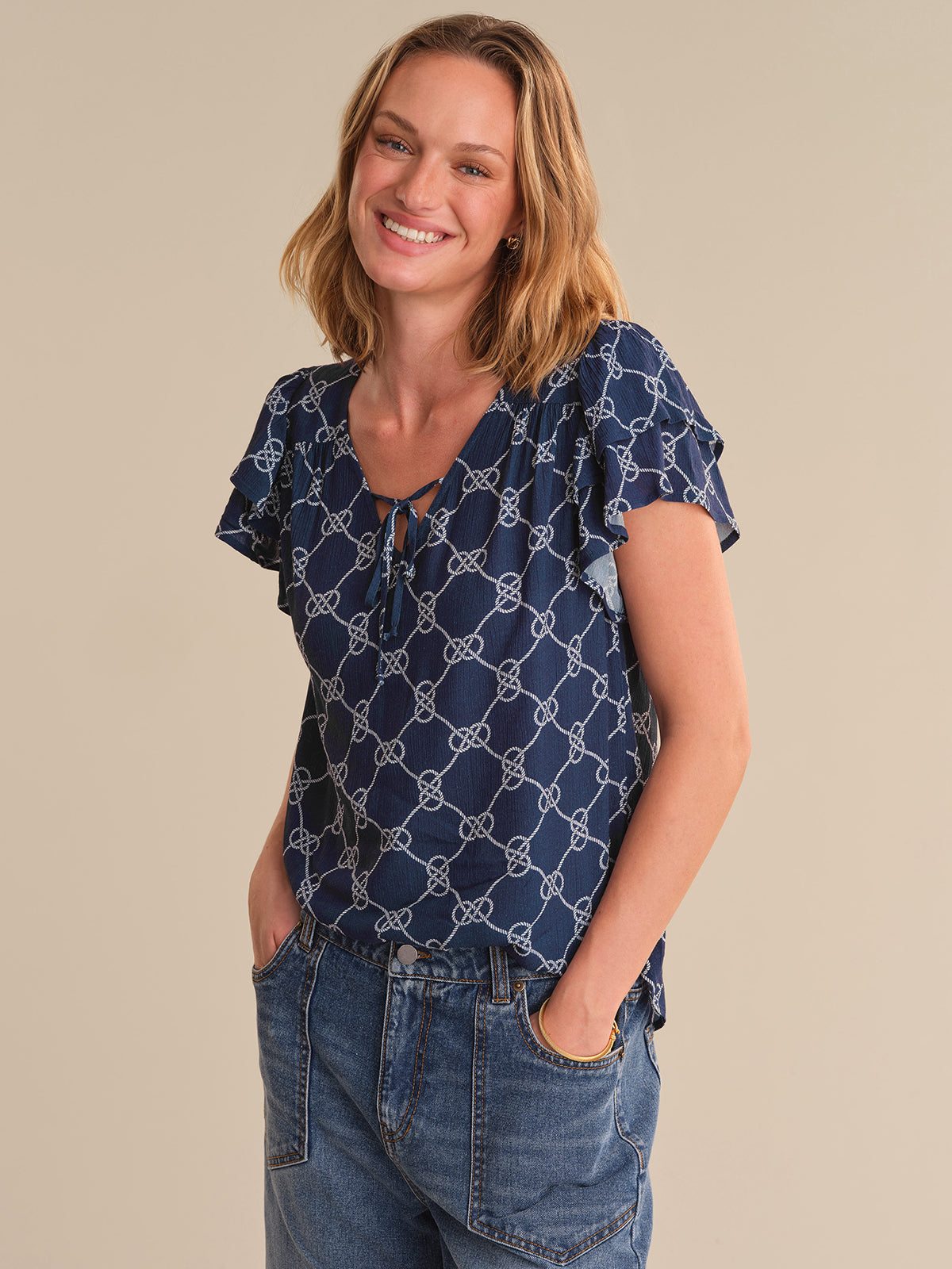 Woman wearing a blue patterned top and jeans on a beige background